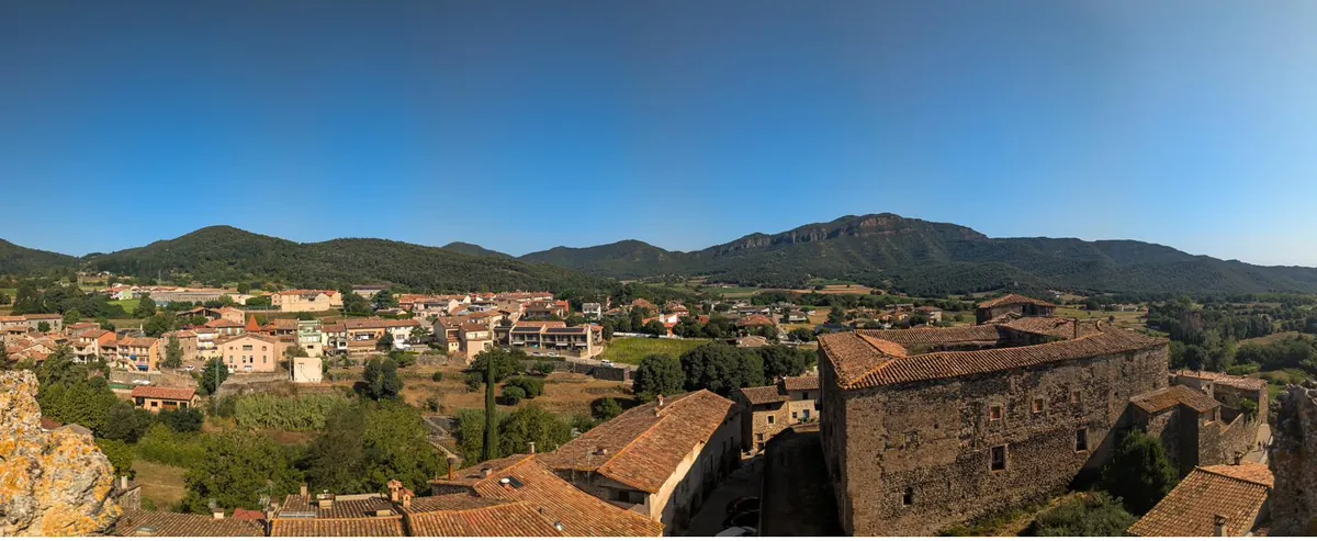 Vista general de Santa Pau des de dalt, amb les teulades del nucli antic i el campanar entre els turons de la Garrotxa.