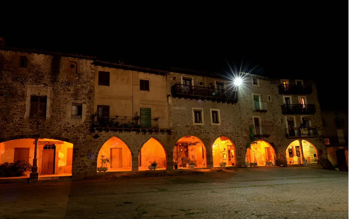 Els porxos de la plaça de Dalt de Santa Pau il·luminats de nit, amb els arcs de pedra.