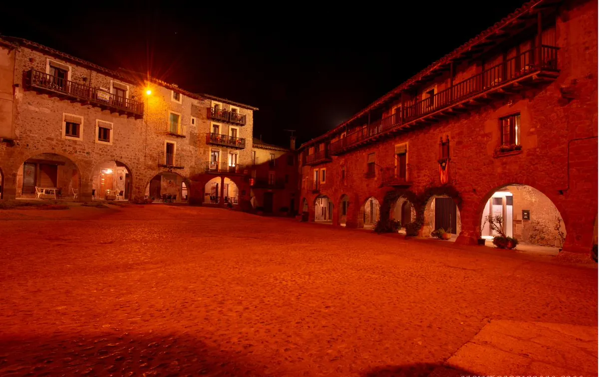 La plaça Major de Santa Pau de nit, amb els edificis porxats il·luminats.